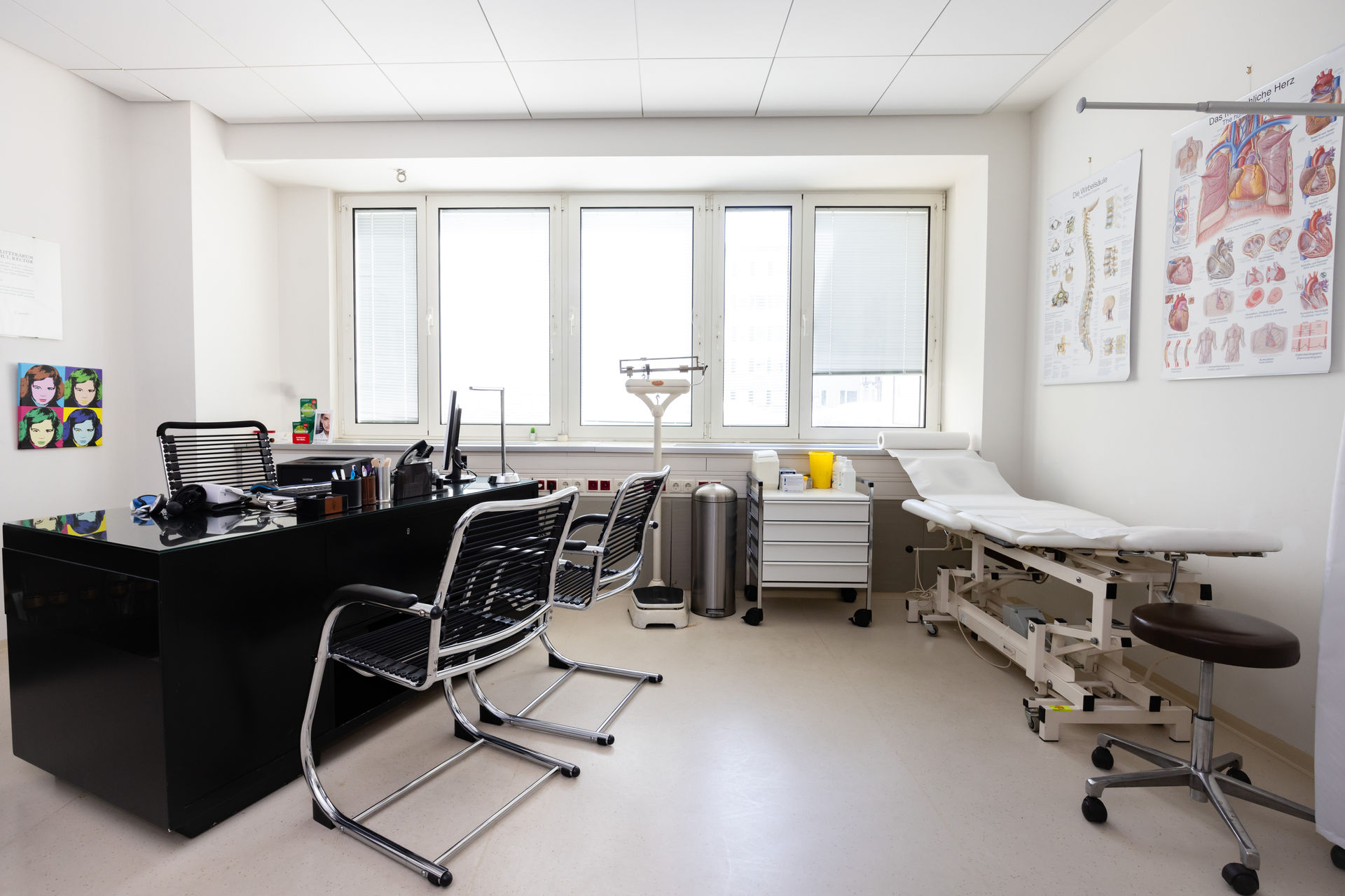 Sprechzimmer mit Schreibtisch, Untersuchungsliege und anatomischen Tafeln